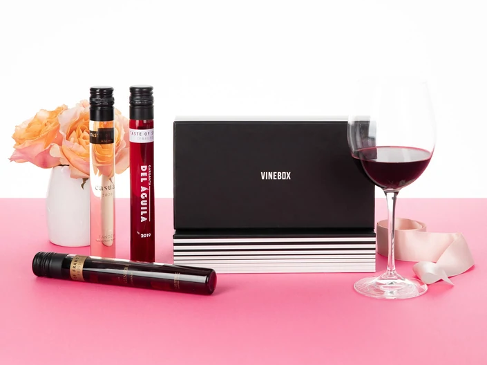 A black box containing plastic tubes filled with wine, aside a glass filled with red wine from Vinebox.