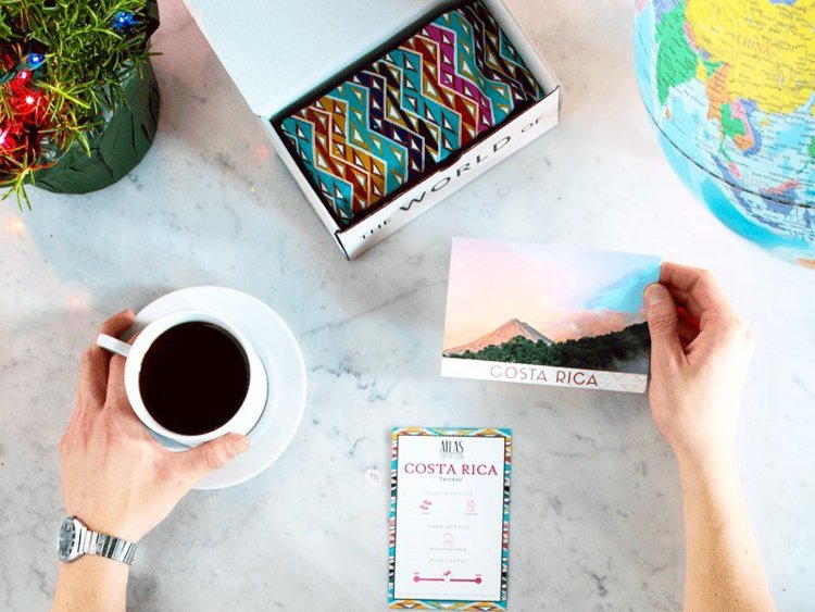 A box of atlas coffee, a post card from Costa Rica, and a hand clutching a cup of coffee.