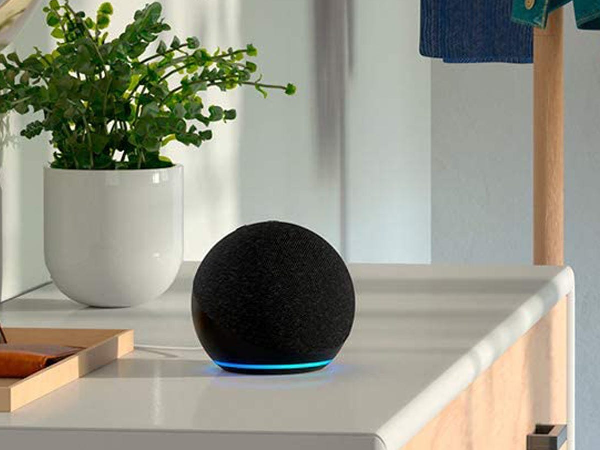 An Amazon Echo Dot 4th gen smart speaker sitting on a table beside a plant.