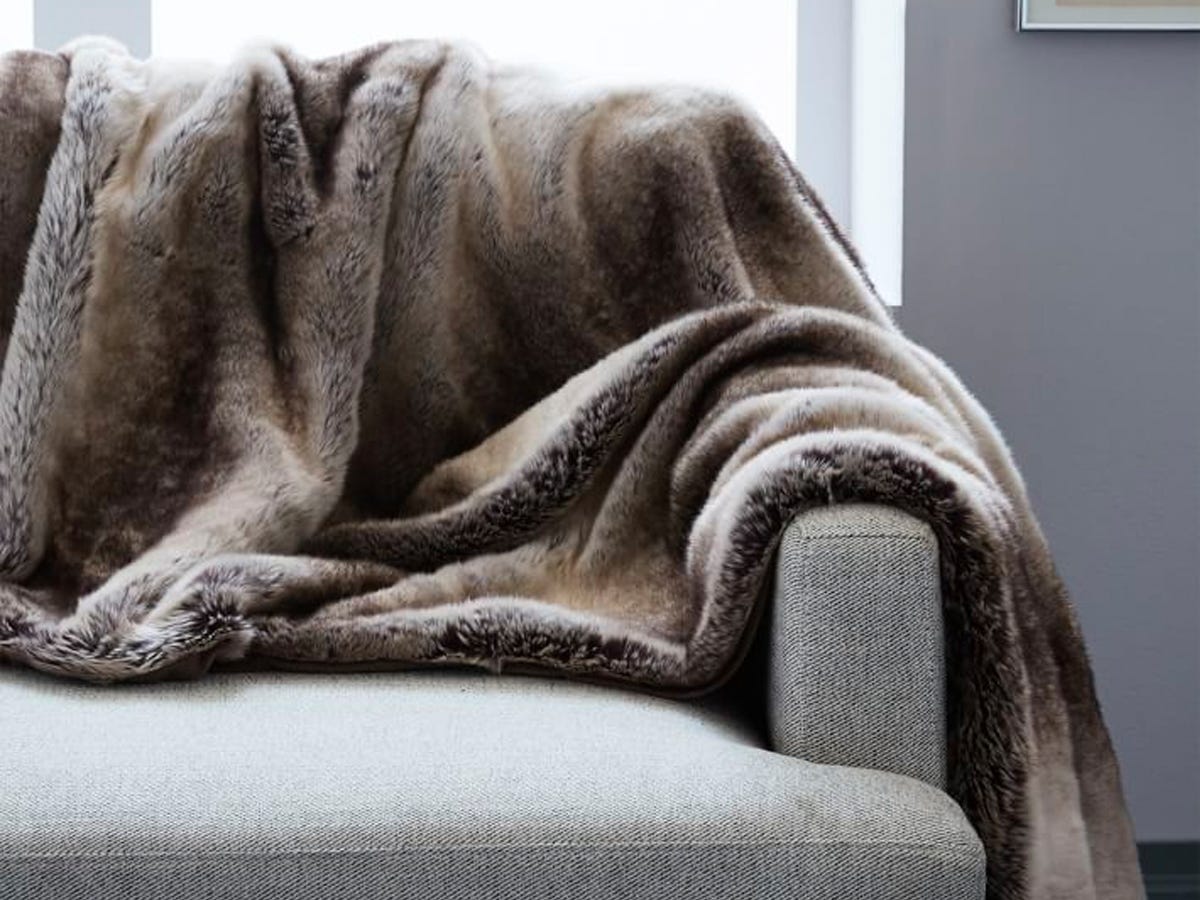 A Faux Fur Ombre Throw blanket draped on a grey couch.