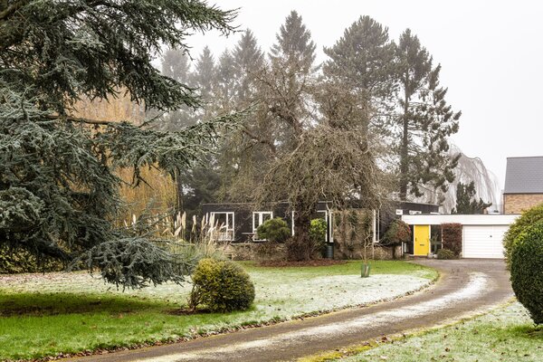 A long, winding driveway creates a welcoming approach to the single-story residence. The bright yellow front door pops against the home's black-stained larch facade.