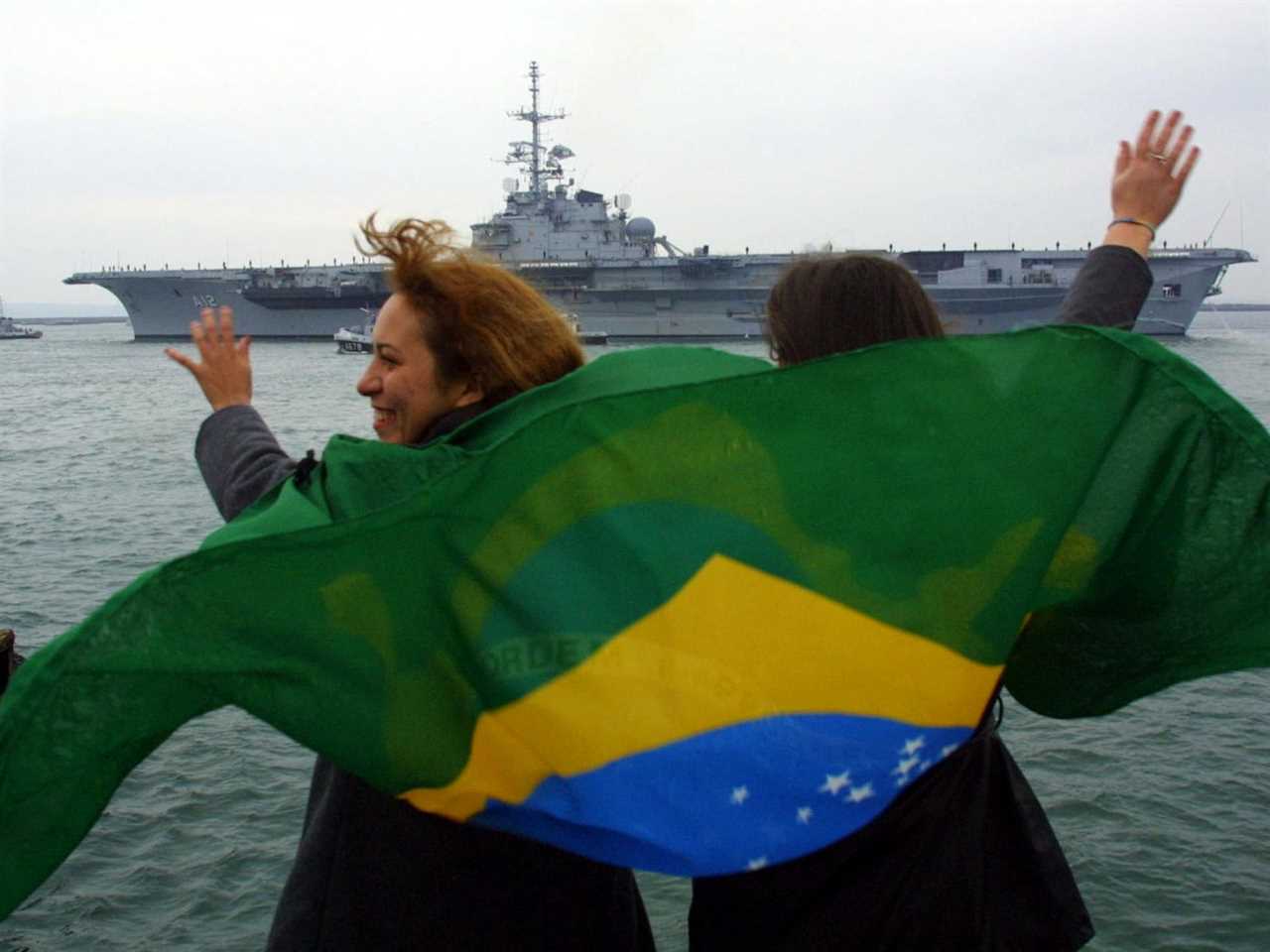 Two Brasilian women wave a national flag as former French "Foch" aircraft carrier, renammed "Sao Paulo" leaves Brest harbour, 01 February 2001, western France.