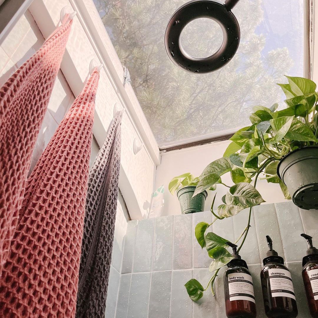 Shower space in van with roof light, circular shower head and bright towels hanging from hooks