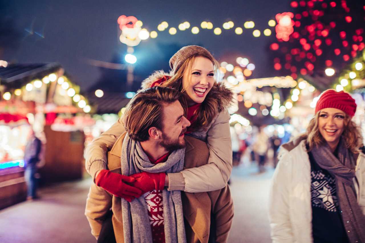 Young couple having fun outdoors in the winter under holiday lights