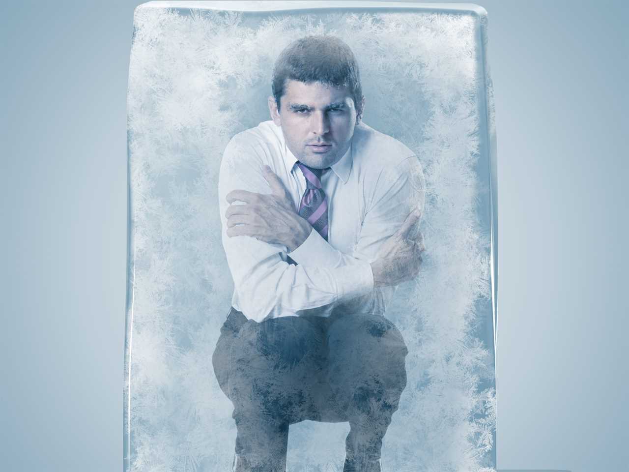 Businessman crouched frozen in an ice space