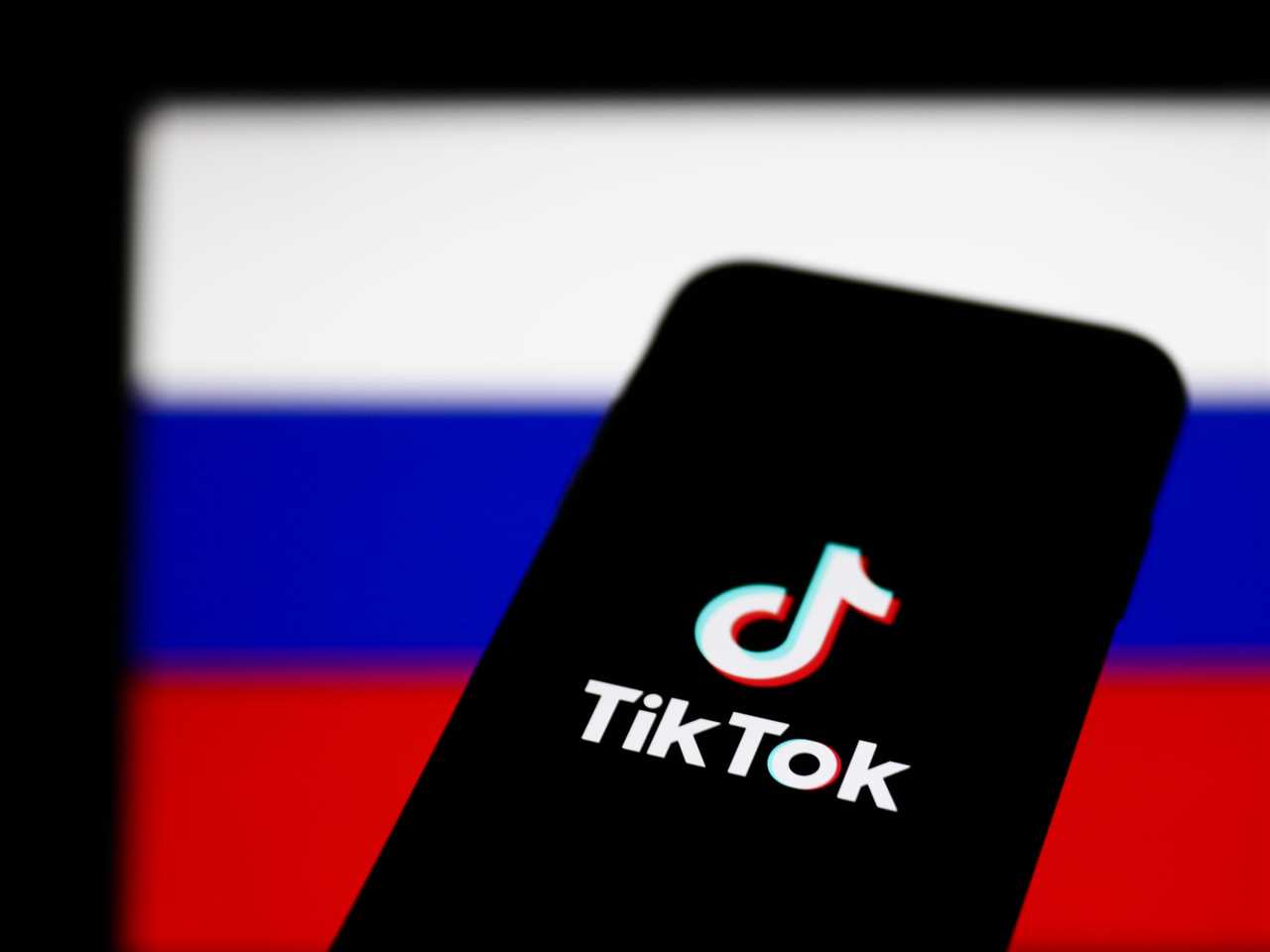 TikTok logo on a phone in front of a Russian flag