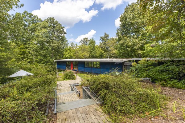 A bright red door pops against the home's blue exterior facade. The remote lot, filled with soaring, shaded trees, enhances the property's sense of privacy.