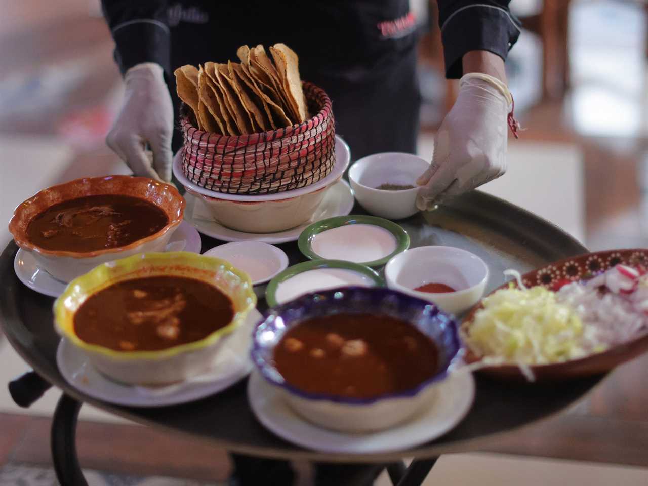 A waiter wearing safety gear to follow sanitary protocols against Covid-19 takes plates of food to serve to customers during a working day at Salon Tenampa on August 22, 2020 in Mexico City, Mexico