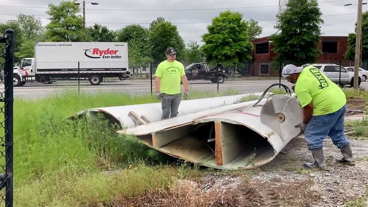 Two men use a circular saw to cut a large wind turbine blade into smaller segments.