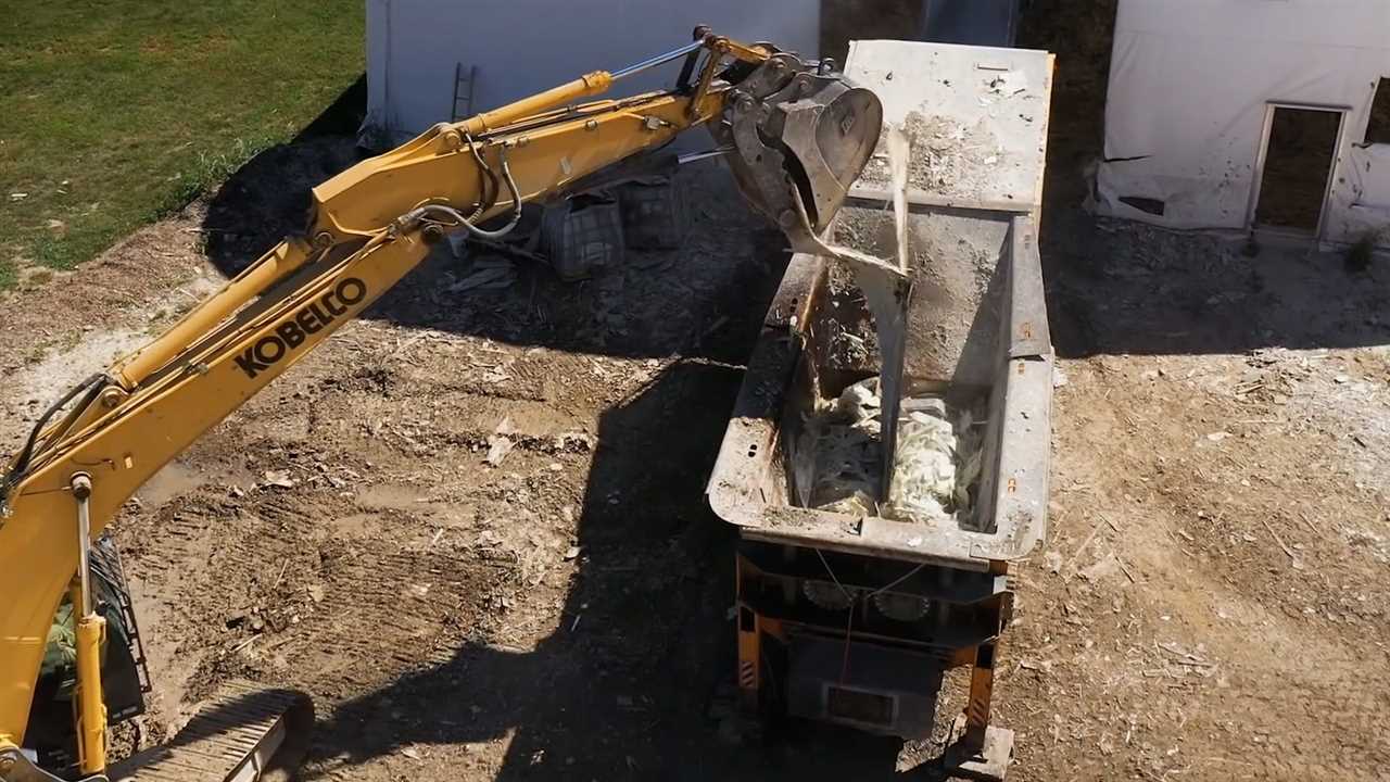 Construction machinery lowers a segment of a wind turbine into a shredding machine.