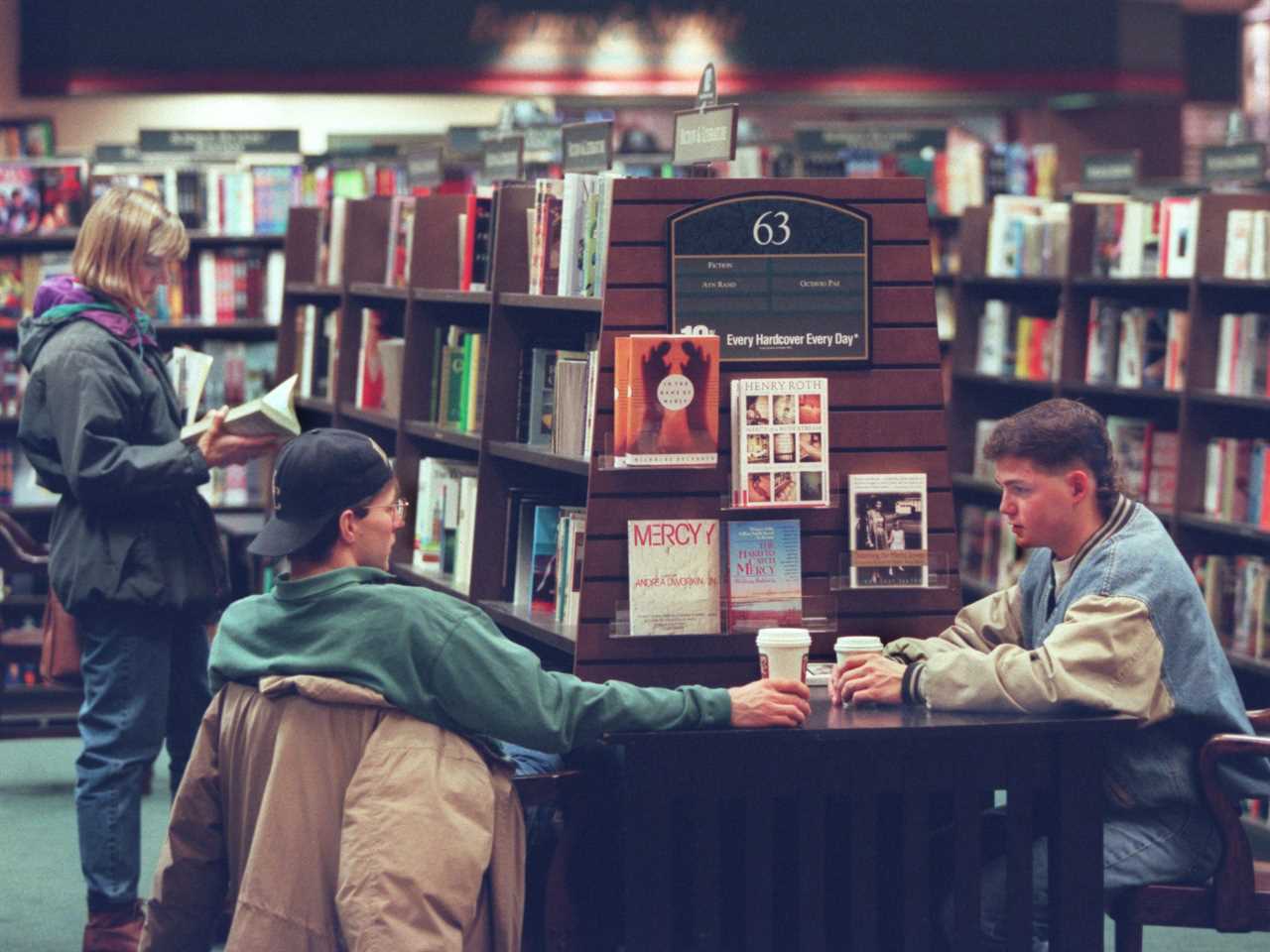 Two men sit with takeout coffee cups while woman browses books at Barnes & Noble store