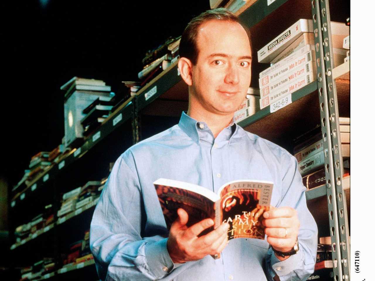 Jeff Bezos holds book and poses against book rack