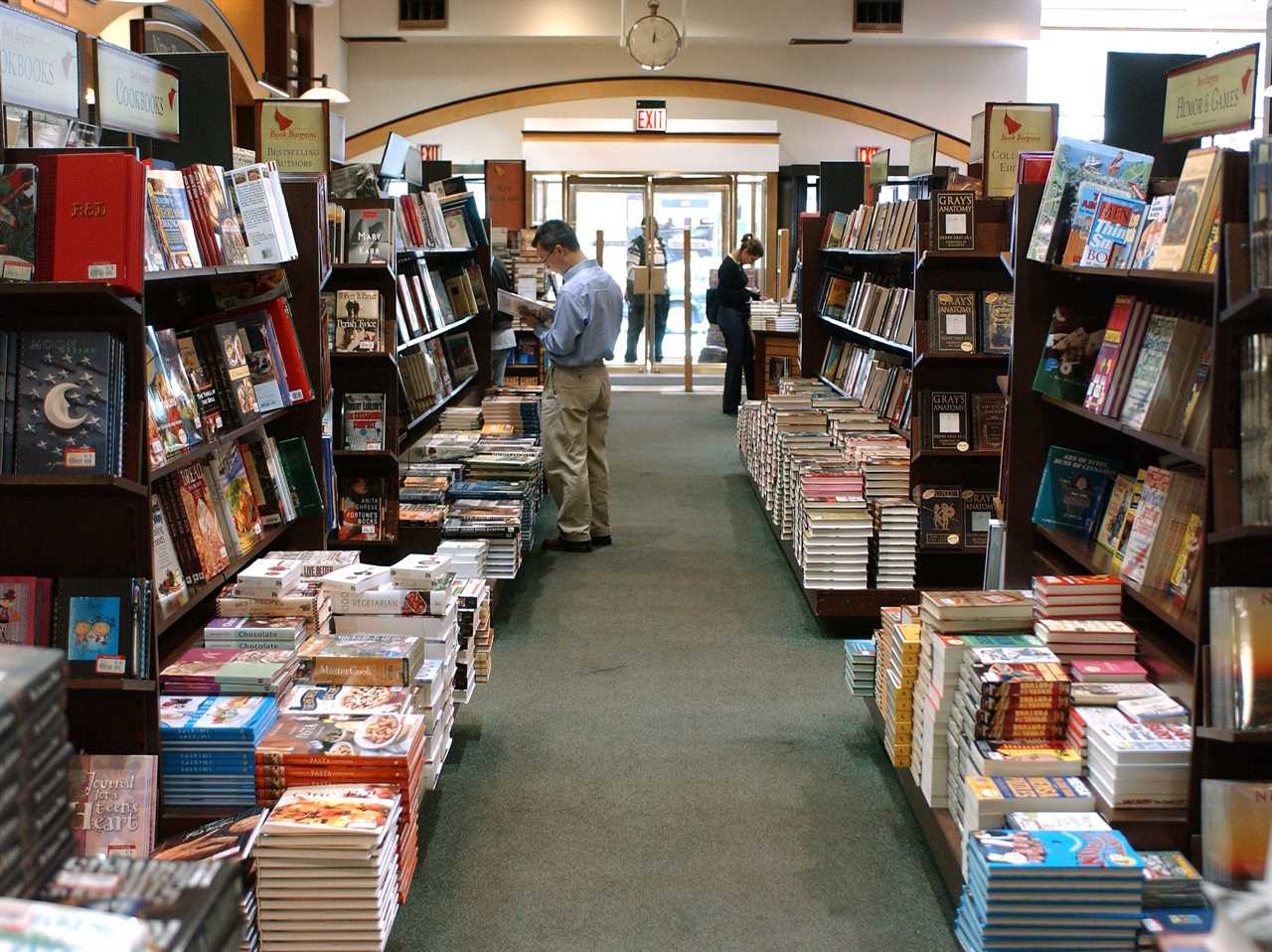 Stacks of Barnes & Noble books on the floor next to shelves while customers shop