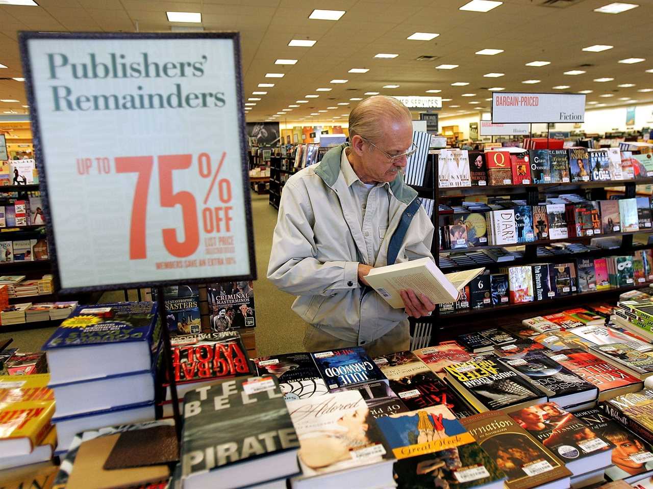 Man looks at book standing at table in Barnes & Noble store with 75% off sign