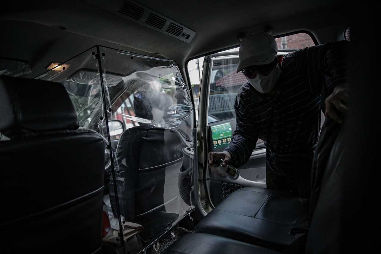 Taxi driver cleans back seat of car.