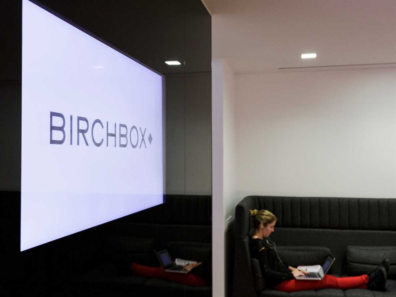 Employee sits working next to sign that says Birchbox inside company headquarters