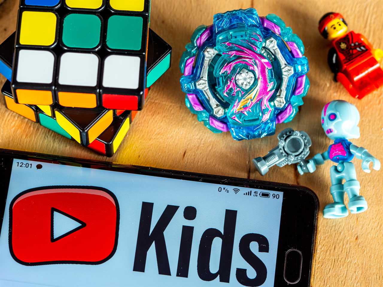 A phone showing the YouTube Kids logo next to toys like a rubiks cube, Lego, and a robot.