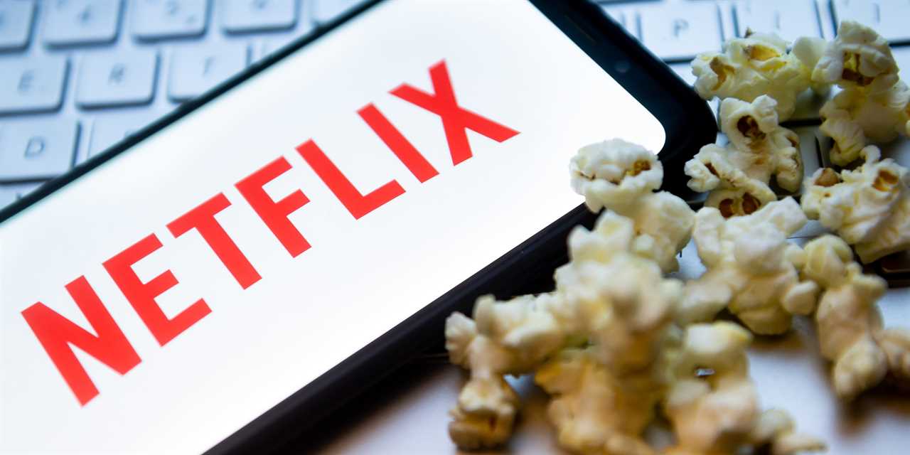 The Netflix logo is displayed on a smartphone with popcorn and laptop keyboard in the background.