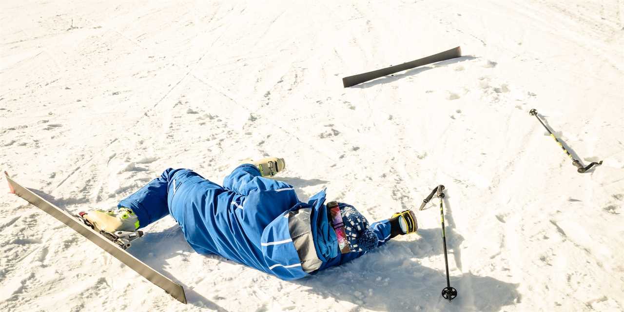 A skier wearing a blue ski suit, helmet, and goggles falls flat in the snow, with a ski and pole left behind.