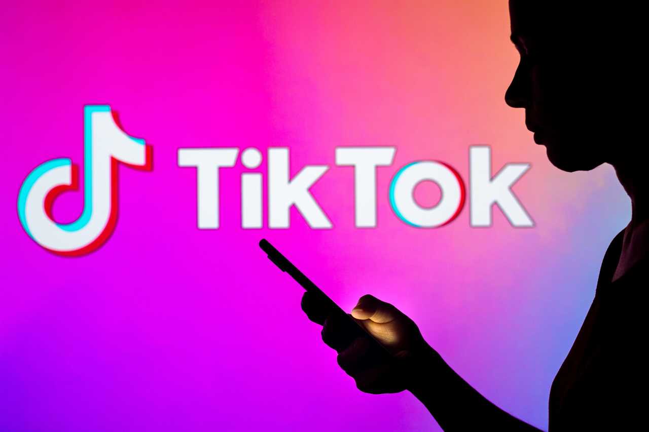 tiktok logo behind silhouette of woman using smartphone