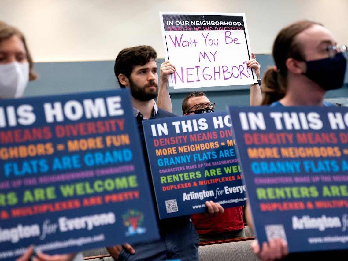 A demonstrator holds up a sign that says "Won't you be my neighbor?", a quote from the children's show Mister Rogers' Neighborhood which promoted welcoming and acceptance between people, during the Arlington County board meeting in Arlington, Virginia, on July 16, 2022.