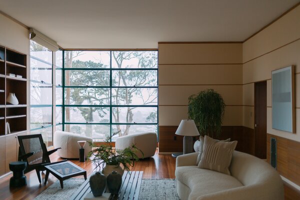 A trove of original details can be found all throughout the residence, including the floor-to-ceiling windows, custom built-in shelving, and blue tiled fireplace  awaiting in the main living room.