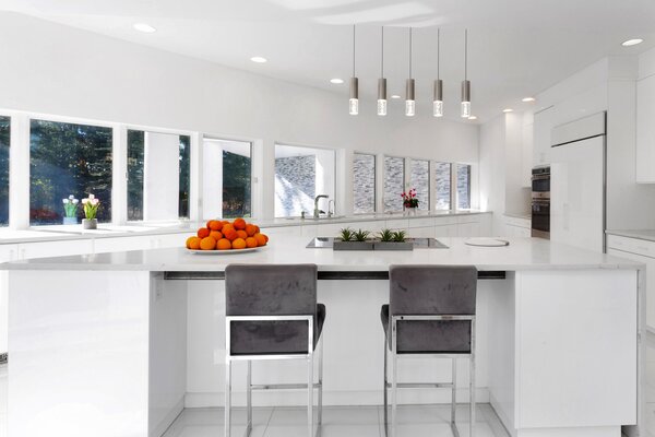 Picture windows stretch across the kitchen, which features stainless steel appliances, long countertops, and an angular central island, complete with barstool seating.