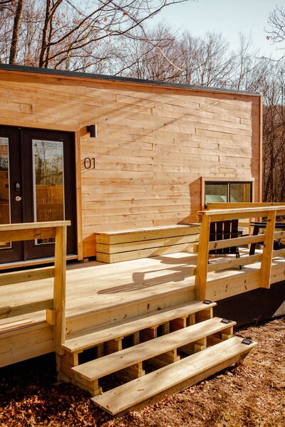 The wood-clad cabin features a large porch furnished with a built-in bench and a fire pit and a pair of Adirondack chairs.