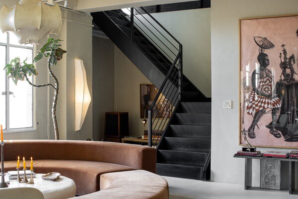 Beyond the curved conversation sofa is a black metal staircase connecting the space with the primary bedroom and office located on the upper level.