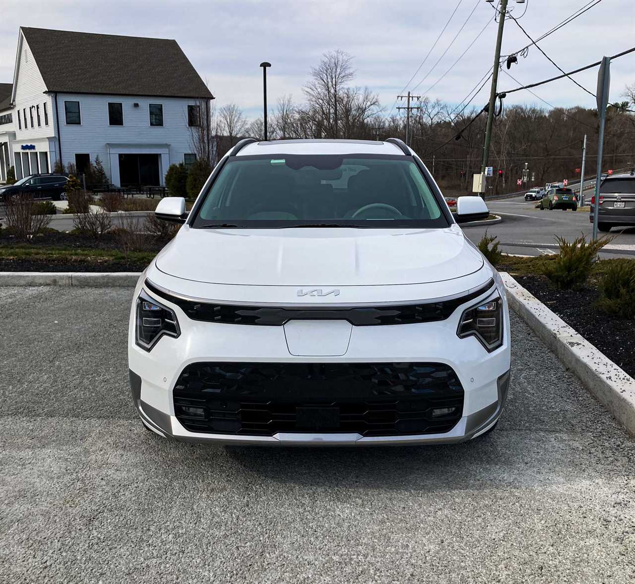 The front of the Kia Niro EV electric SUV against an overcast sky and Dunkin' Donuts in the background.