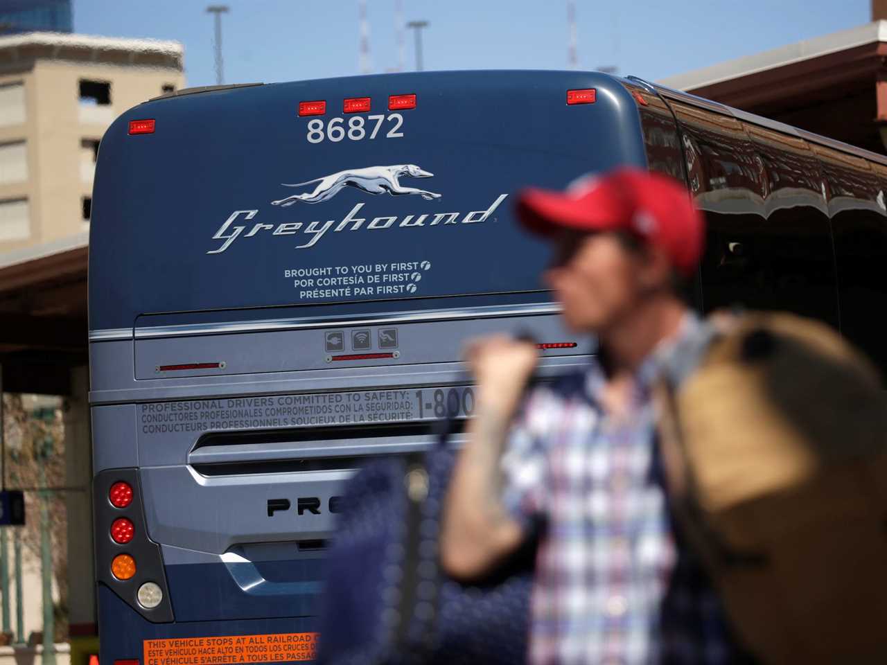 A person wearing a hat carrying a bag while a Greyhound bus is in the back.