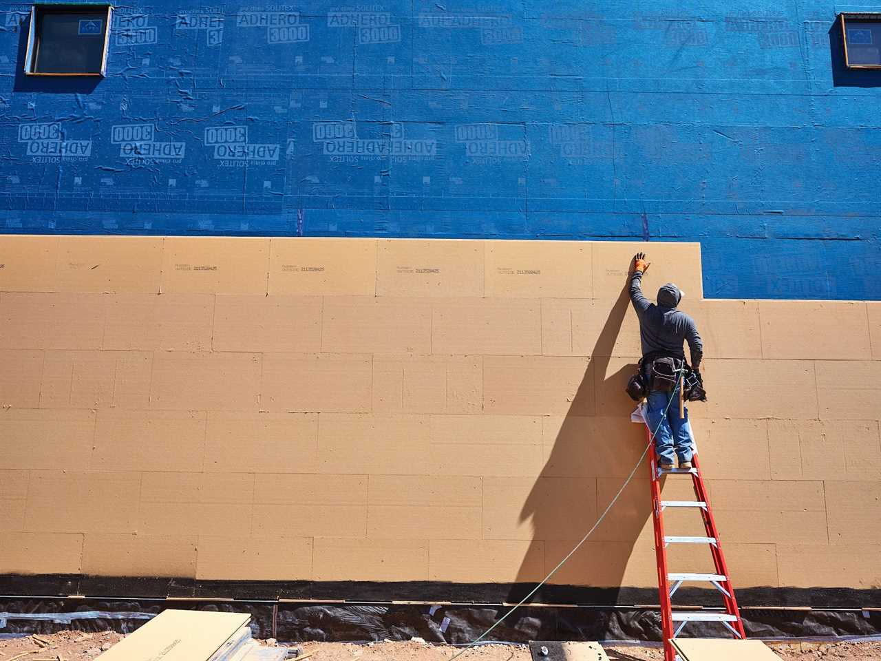 A construction worker installing an insulating membrane on a house.