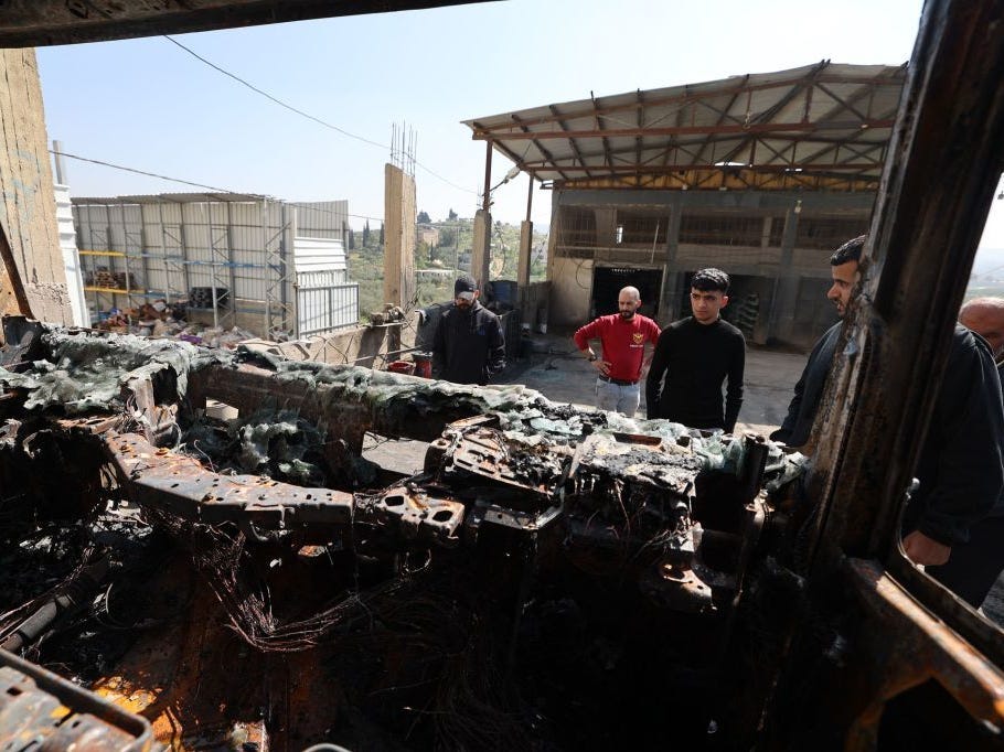 Men inspect a burnt vehicle following a reported attack by Israeli settlers on the Palestinian town of Huwara in the occupied West Bank on March 28, 2023.