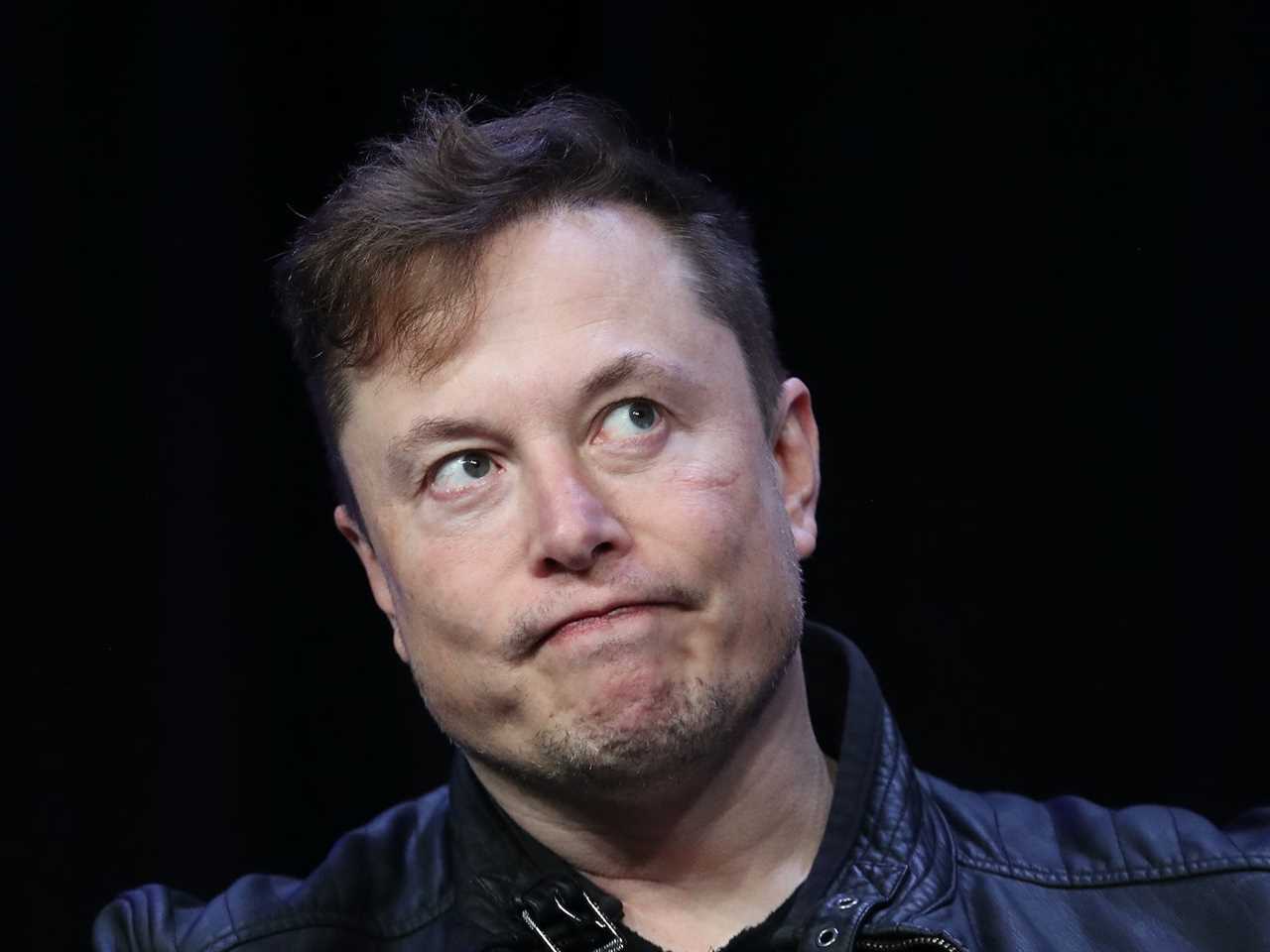 Elon Musk grimaces while looking off to side against black backdrop