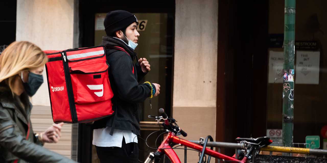 A DoorDash rider with his bike and delivery pack on his back exiting a NYC restaurant in winter.