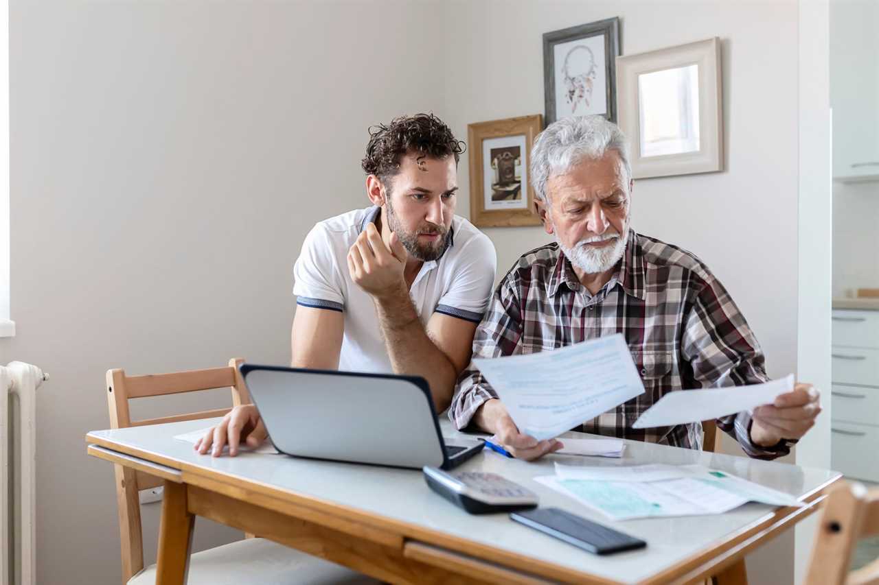 elderly man and adult son go over some financial documents while sitting at a table