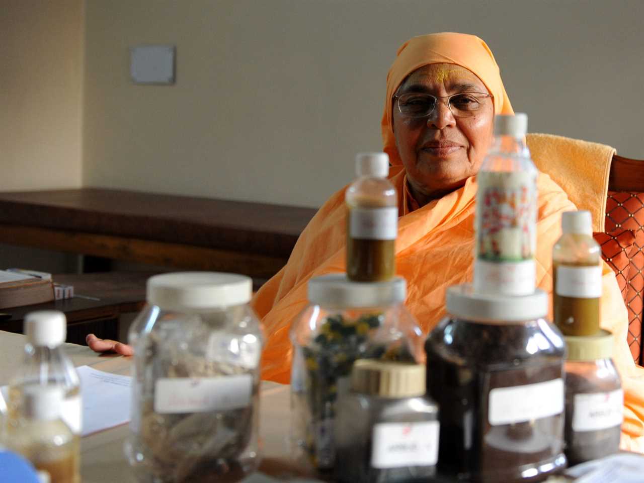 A woman sits behind medicine made from cow urine that is believed to treat cancer and kidney problems.