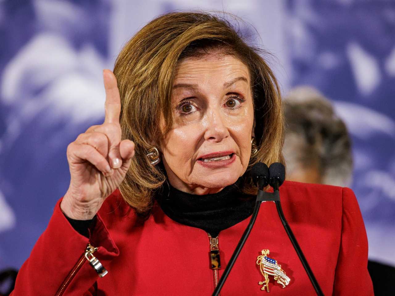 House Speaker Nancy Pelosi, her right hand held nearly at eye level, index finger pointed towards the sky, speaks to reporters outside Union Station in Washington, DC.