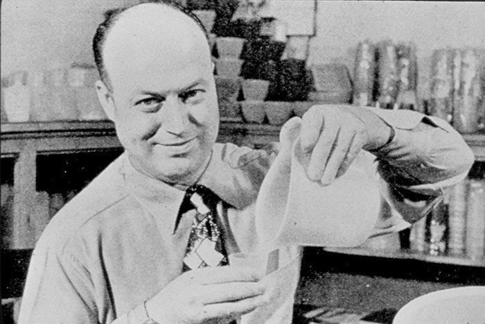 Earl Tupper, inventor of Tupperware, appears in a shirt and tie holding one of his containers in a black-and-white photo.