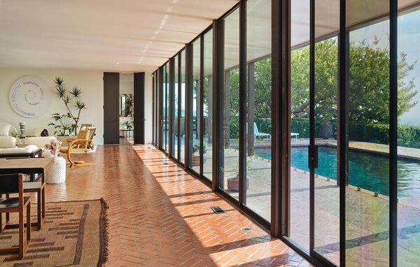 A glass wall spans across the main living areas, framing striking views of the pool and city skyline beyond. Floor-to-ceiling doors enhances the home's overall sense of space.