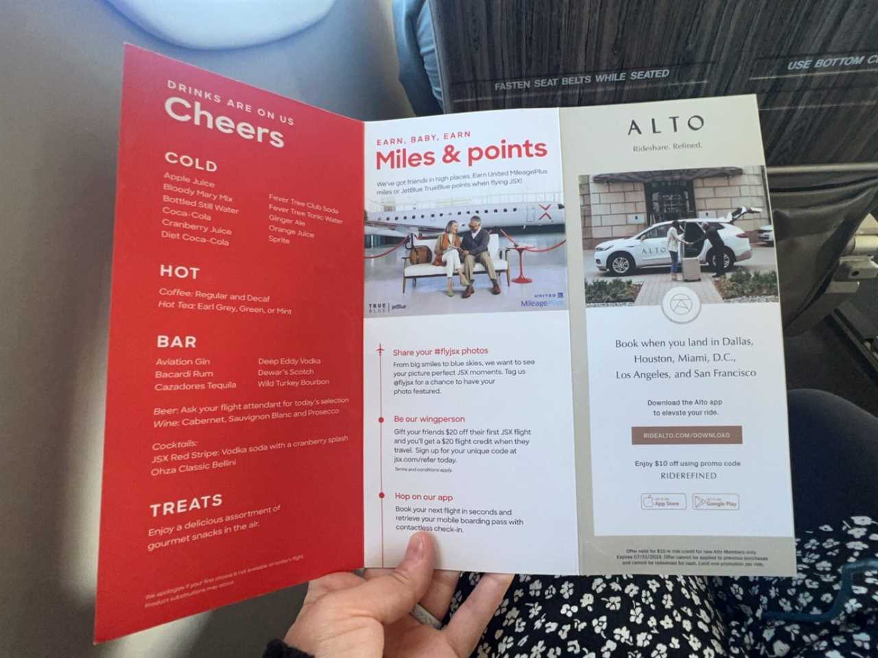 The author holding a red and white menu displaying complimentary drink options and a section about the rewards passengers earn when flying with JSX.