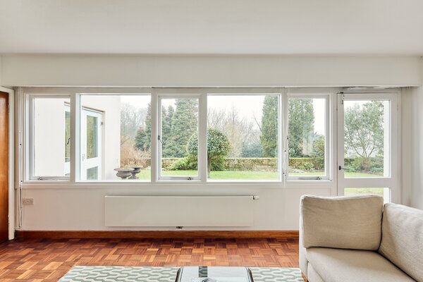 Refinished parquet flooring runs throughout the living room, where a wall of windows frame picturesque views of the backyard garden.