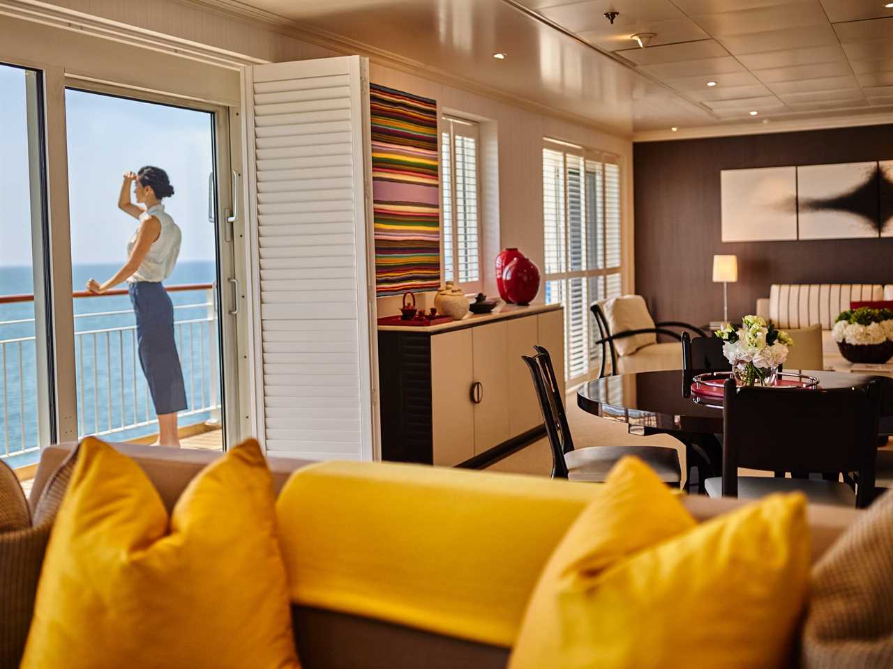 A view from inside a stateroom where a woman stands on a balcony looking out to sea.