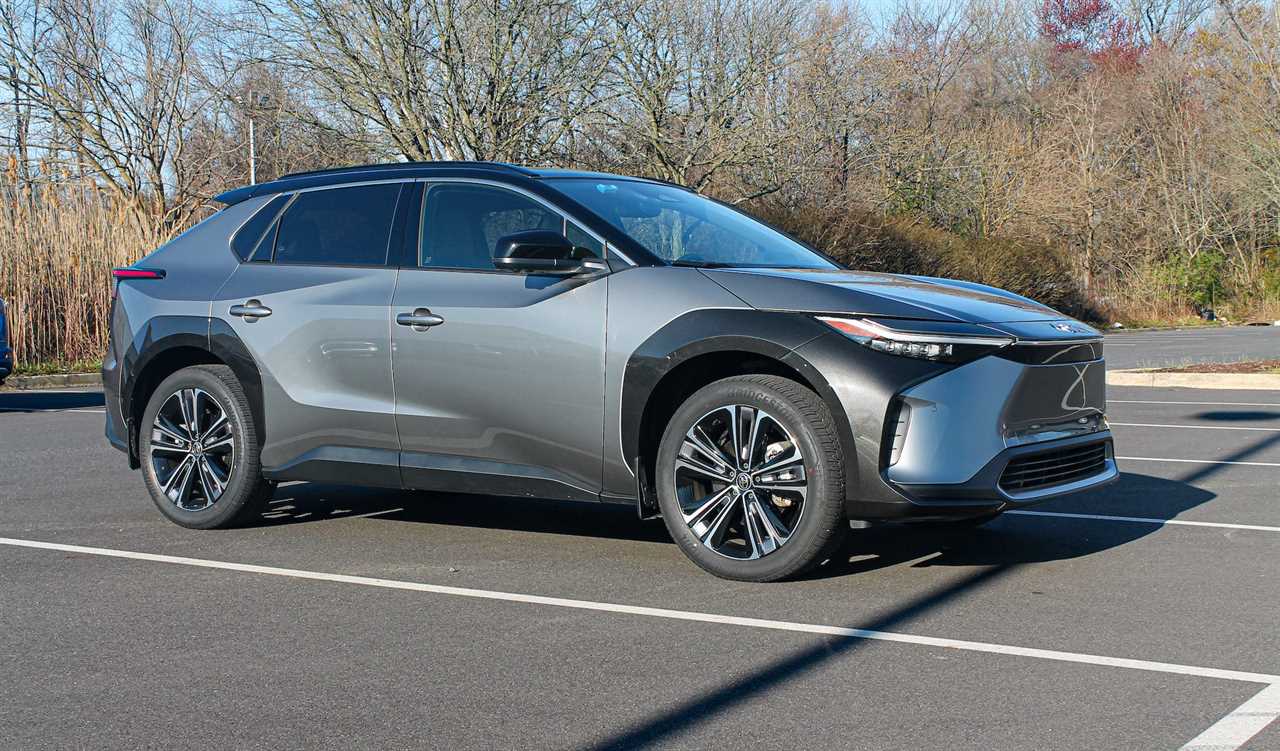 A silver 2023 Toyota bZ4X AWD Limited in a parking lot, with trees and a blue sky in the background.