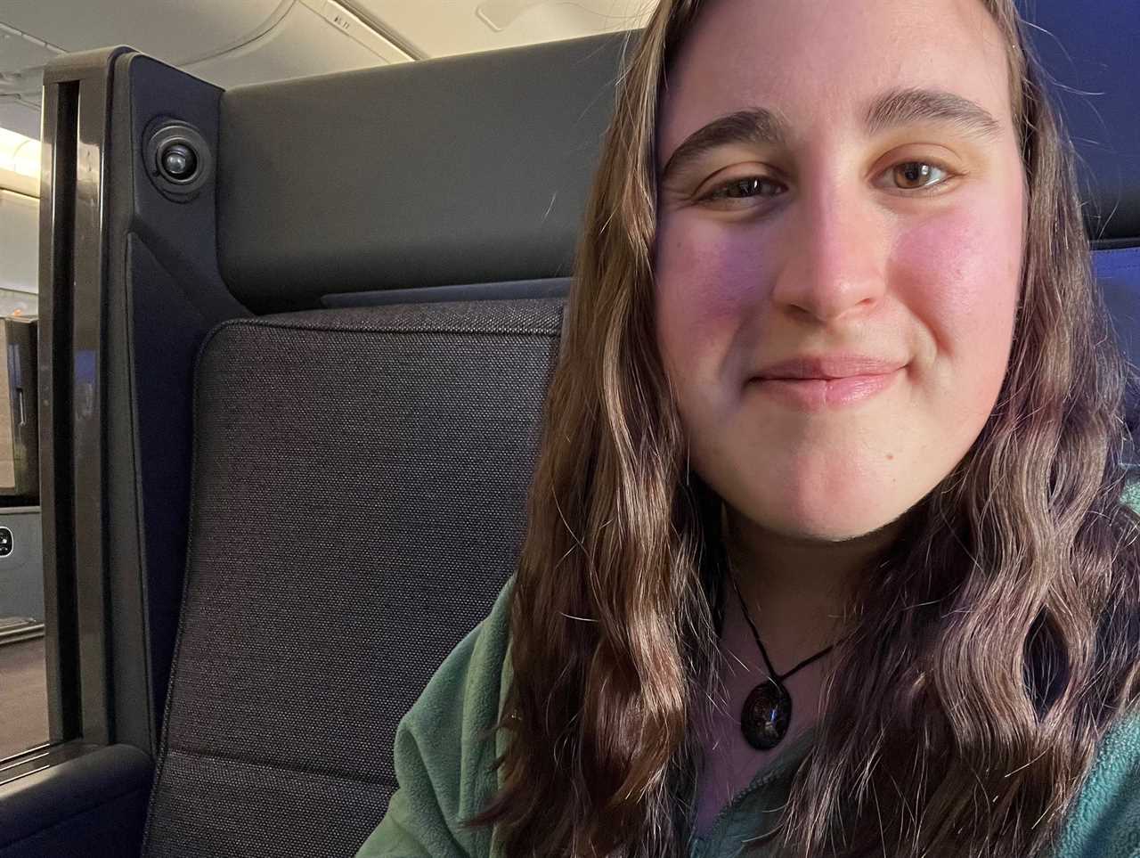 A selfie of the author sitting in "The Room" business class wearing a green sweatshirt.