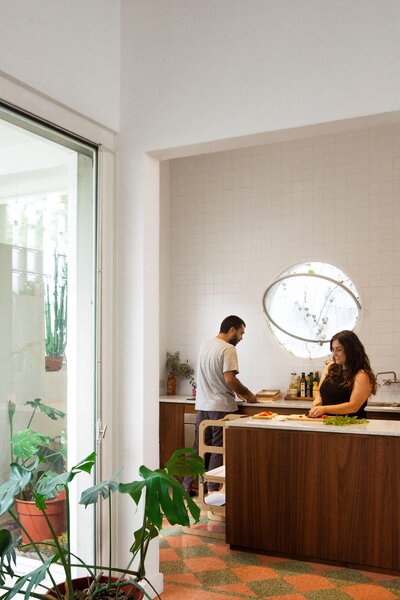 Vines climb along the frame of a new circular window in the kitchen. The pink and green floor tiles are original.