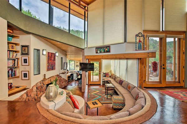 The glass entrance leads to the main living area where a long, curved built-in sofa provides an idyllic conversation starter. A stone fireplace complements the red-hued flooring.