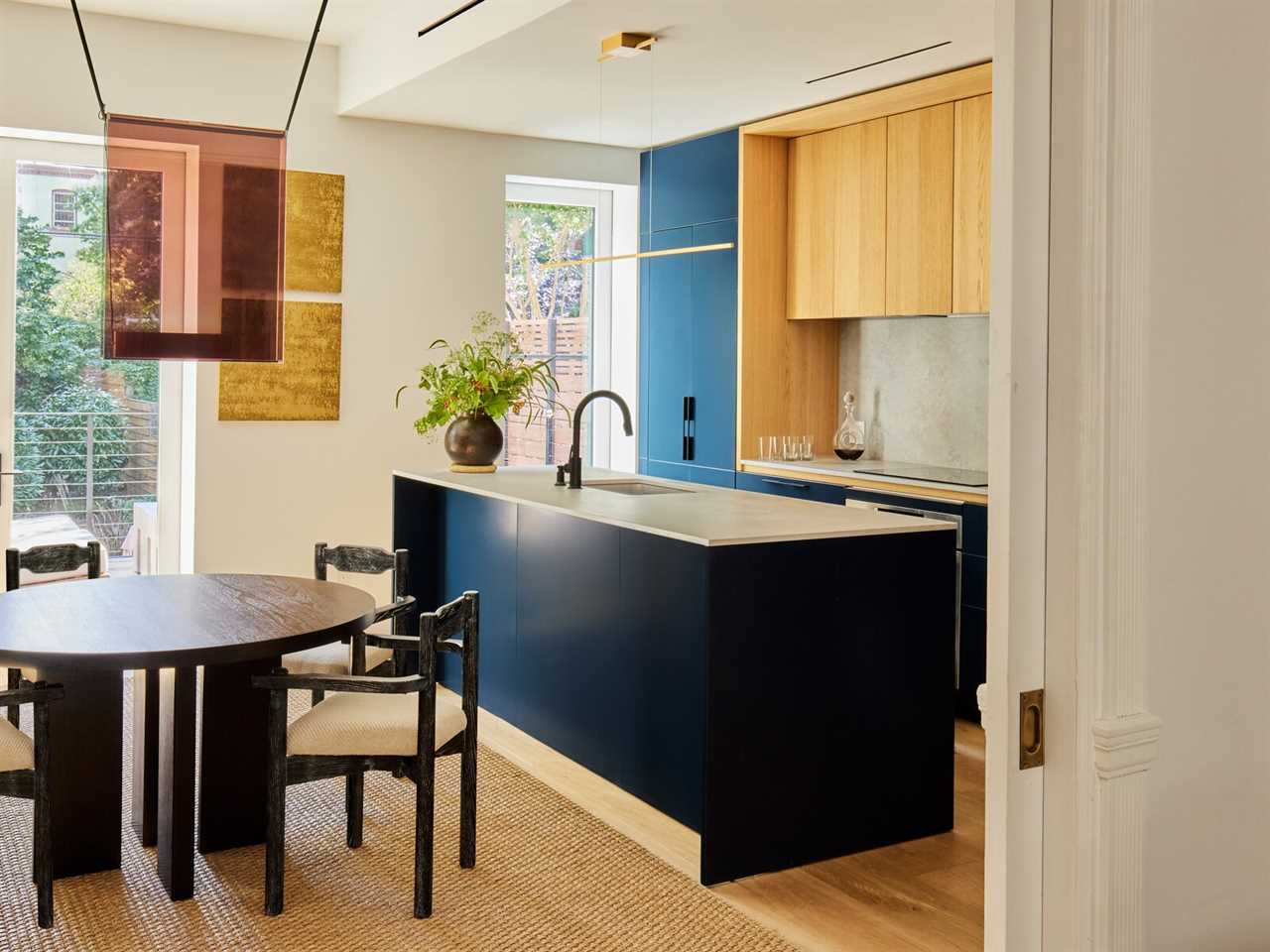 In the dining room, Guillerme et Chambron armchairs from Maison Gerard surround a CB2 table. The ceiling light is by Lambert &amp; Fils. In the kitchen, rich blue cabinetry with wood details from GD Arredamenti is topped with a Caesarstone 