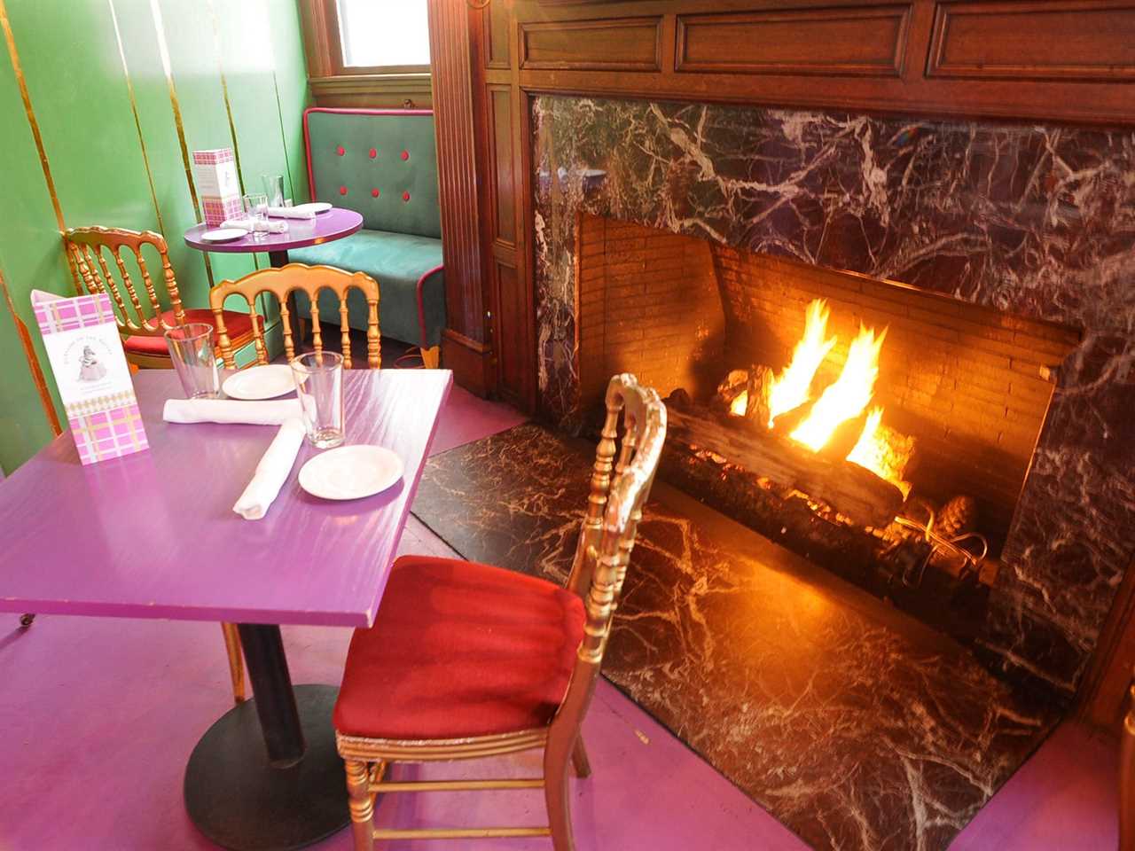 Pink tables and green walls in front of a fireplace at a restaurant