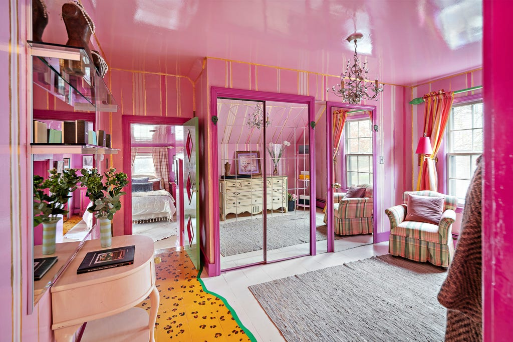 A dressing room with pink and gold walls with mirrored closet doors